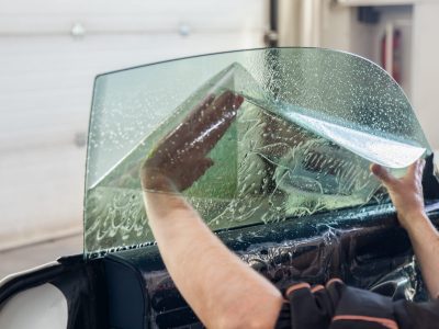 The wizard for installing additional equipment sticks a tint film on the side front glass of the car and flattens it by hand to fit the glass with a greenish tint in the auto service.